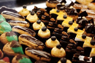 A closeup of an assortment of French pastries, including chocolate-covered eclairs and green-tinted crVoisins, arranged on display at the bakery's counter. The focus is on intricate details like shiny black chocolate lines or glossy yellow cream filling in each pastry. This scene captures the vibrant colors and textures that make these mini confections one-of-a-kind pieces of artistry in the style of French pastry artists.