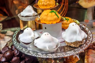 Halloween themed cupcakes with ghost and pumpkin designs, served on an ornate silver tray at the Italian tea shop 'Villa di due Gregori' in Rome's Old Town. The cupcakes were photographed using focus stacking with light white and orange lighting for product photography with a macro lens at high resolution to show very detailed, hyper realistic designs in the style of super realistic art. The photography was done with natural lighting for a professional and studio style with sharp details and beautiful imagery.