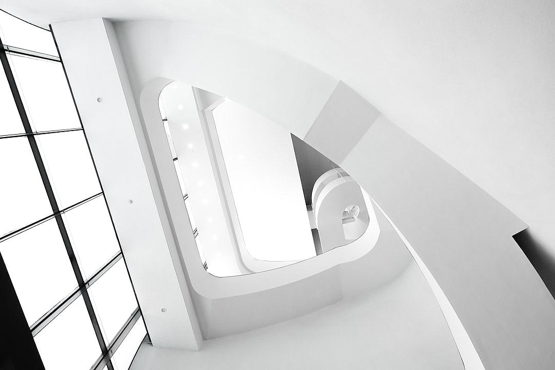 minimalist white interior, white spiral staircase, black window frames, high angle view, in the style of Leica M6 Monochrom with SummiluxMV 50mm f/2 ASPH lens, bright daylight, architectural photography, architectural detail, architectural design magazine cover style