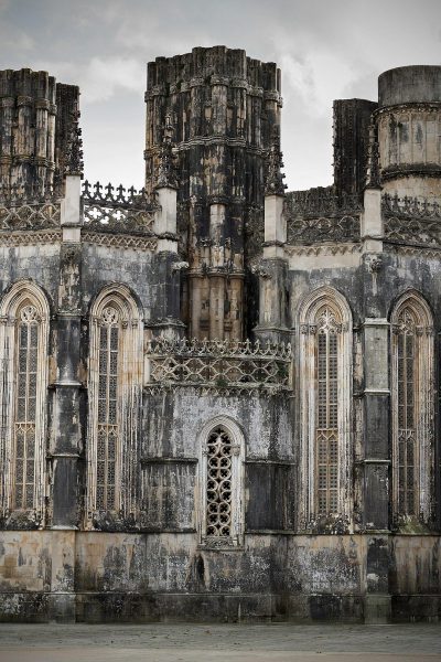 front view of the main facade of B Marias Monastery in TotaLumbar, Portugal, in the style of a postapocalyptic scene, with dark gray and light beige colors, in a symmetrical composition, featuring gothic architecture in a medieval style, with professional photography, color grading, retouching, HDR techniques, achieving a hyperrealistic and cinematic lighting effect, for an architectural photo shoot.