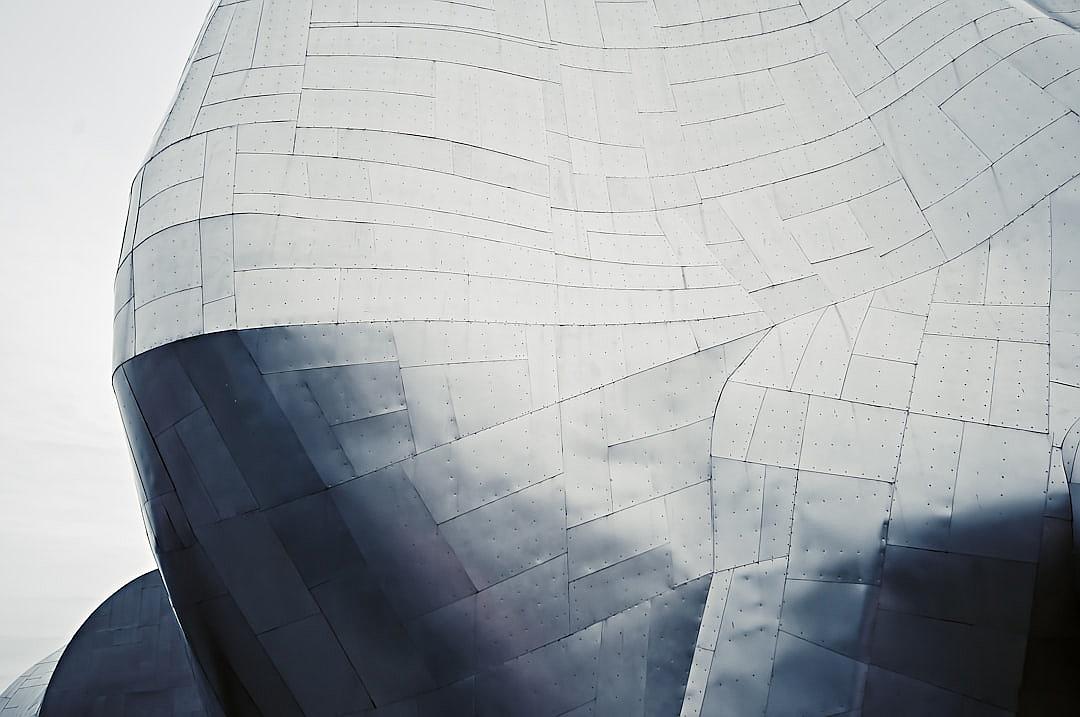 A close-up shot of the sleek, stainless steel exterior of [Frank Gehry](https://goo.gl/search?artist%20Frank%20Gehry)’s architecture at Disney plaster in Los Angeles. The photo captures intricate details and textures on its surface against a white sky background. Shot with a Sony Alpha A7R IV for sharp focus and depth. Soft natural lighting enhances the minimalist aesthetic. A Canon EF lens at 24mm f/8 was used.