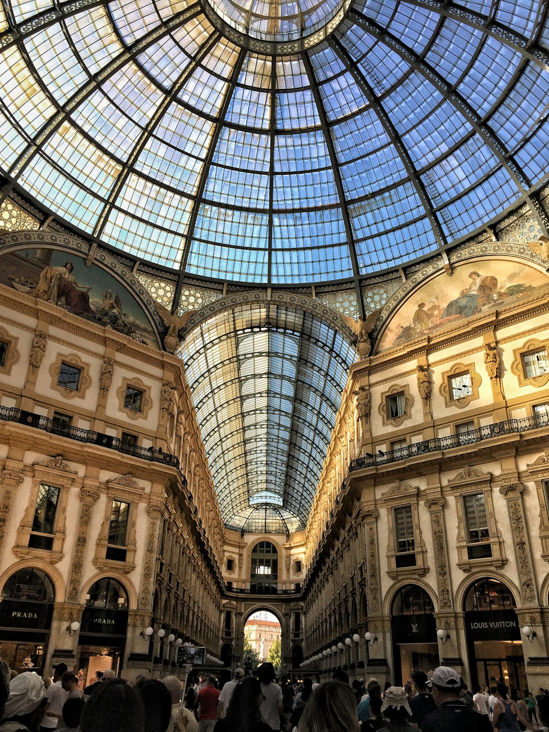 the vittorio emanего galleria in Milan, Italy with the glass dome ceiling and people walking around inside of it. The building has several luxury stores on its ground floor including prada and louisvuitton store. It is sunny outside and there’s lots of natural light coming through the skylight roof, which makes for an amazing photo –ar 3:4