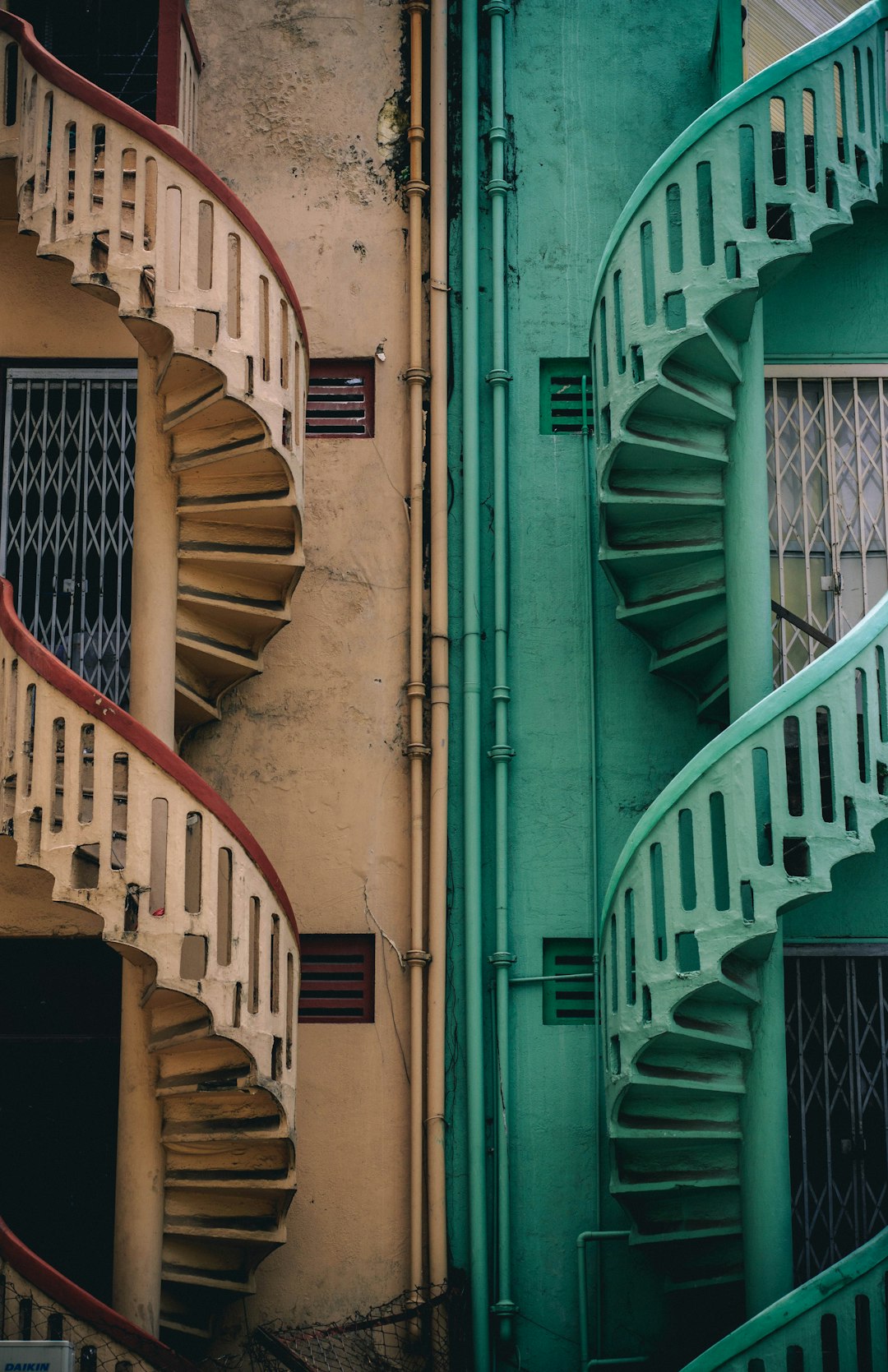 A photo of two spiral staircases, one in light green and the other in dark red, flanked by pastel colored buildings in Singapore’s HDB flats. The ultra realistic photography is in the style of Singaporean artist hdb ultra realistic photography. –ar 41:64