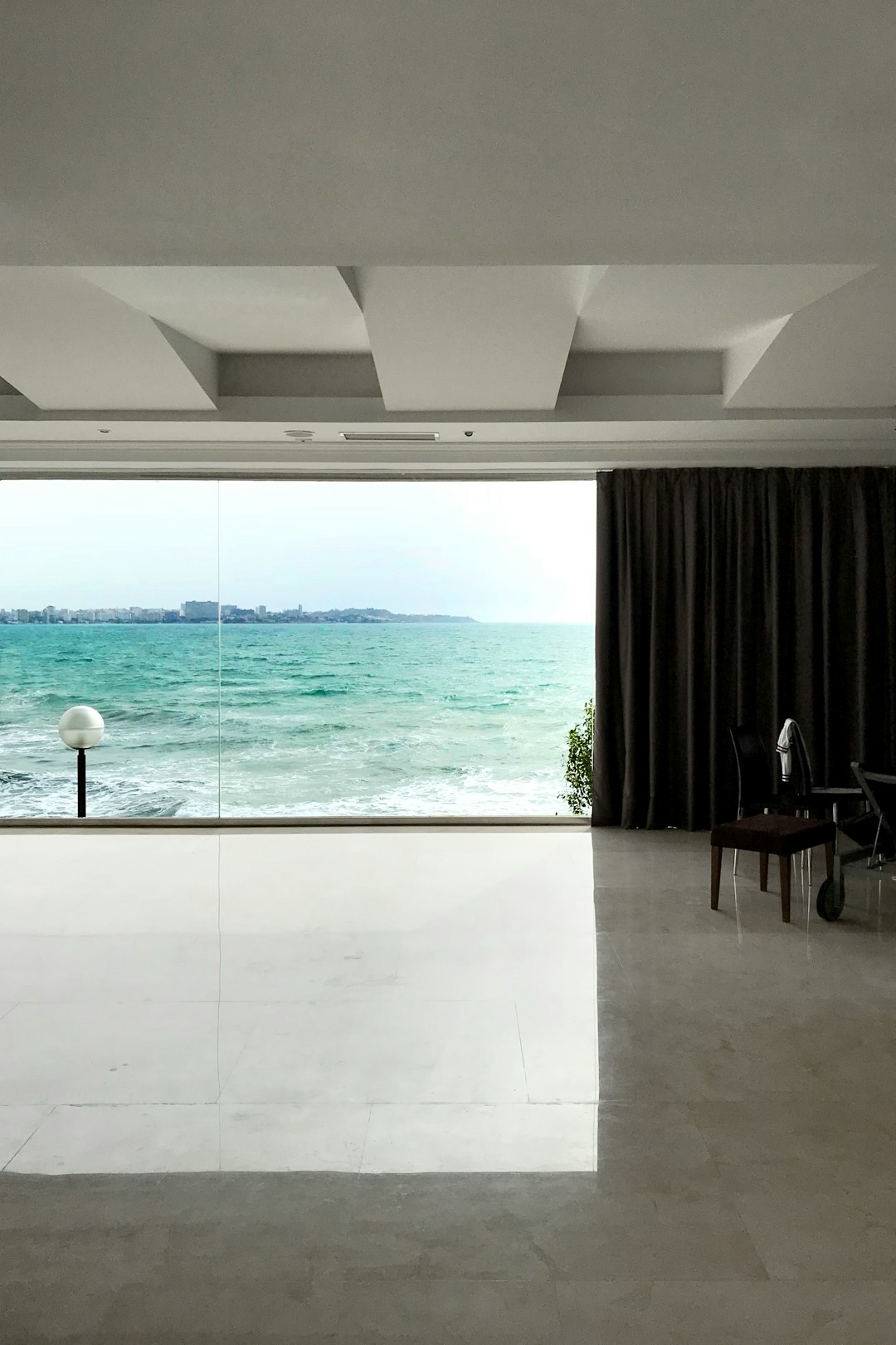 A minimalist interior design, large windows with a view of the ocean, white marble floor and grey walls, modern furniture, black curtains, a large window on one side showing an open sea view, a cinematic shot, natural light.