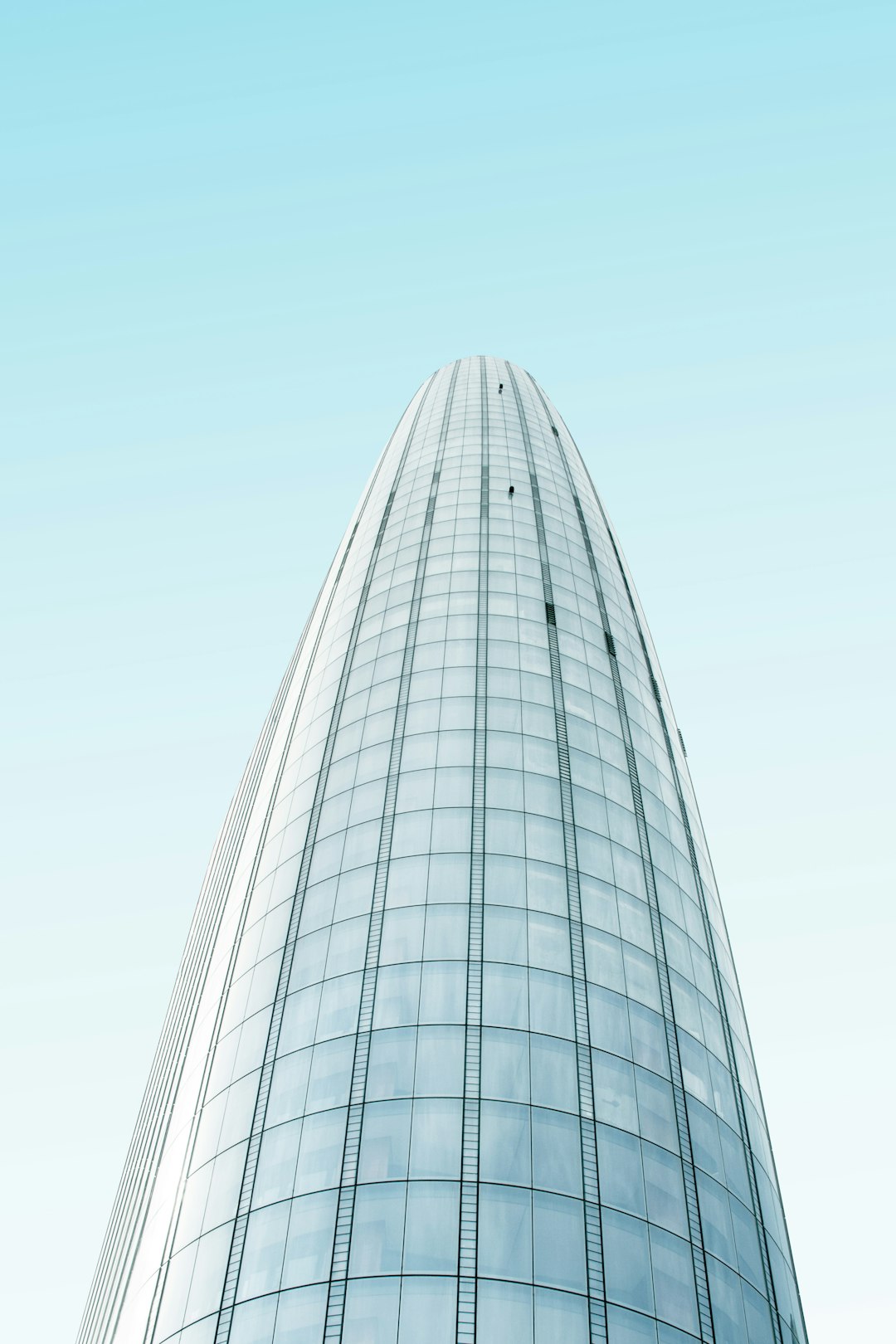 Low angle shot of a glass skyscraper, white sky background, minimalist photography, in the style of Fujifilm Pro 800Z, smooth curves, light blue and dark gray, clear skies with no clouds.