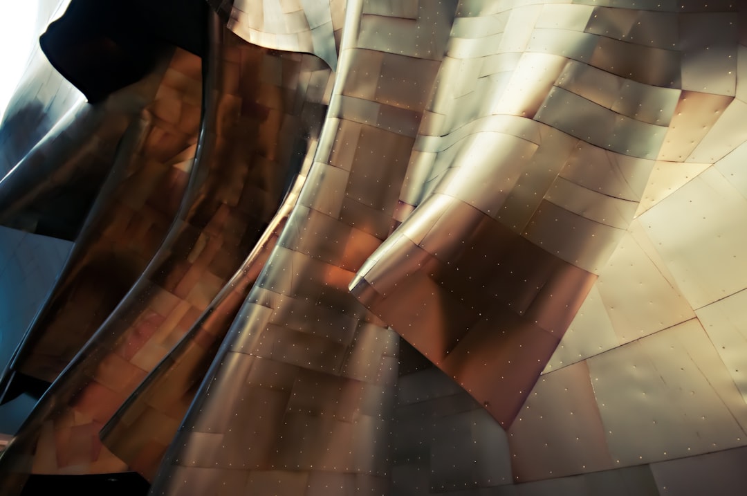 Close up of the exterior wall cladding made from copper and stainless steel, designed in the style of [Frank Gehry](https://goo.gl/search?artist%20Frank%20Gehry) at the well lit interior is visible through one side of it, in Seattle’s decoration museum. –ar 128:85