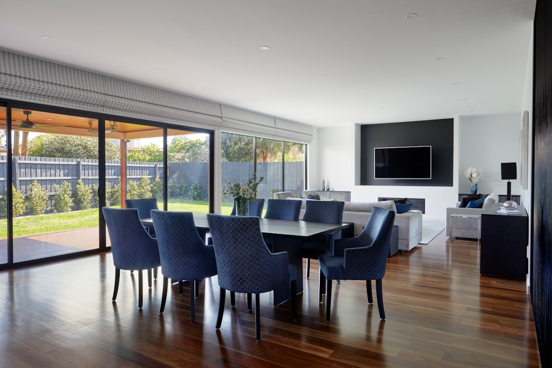 Sleek dining room with dark blue chairs, white walls and sliding doors leading to the backyard in an Australian suburban home. The interior design has a modern minimalist style with a large flat screen television on the wall above the sofa, in the style of minimalist.