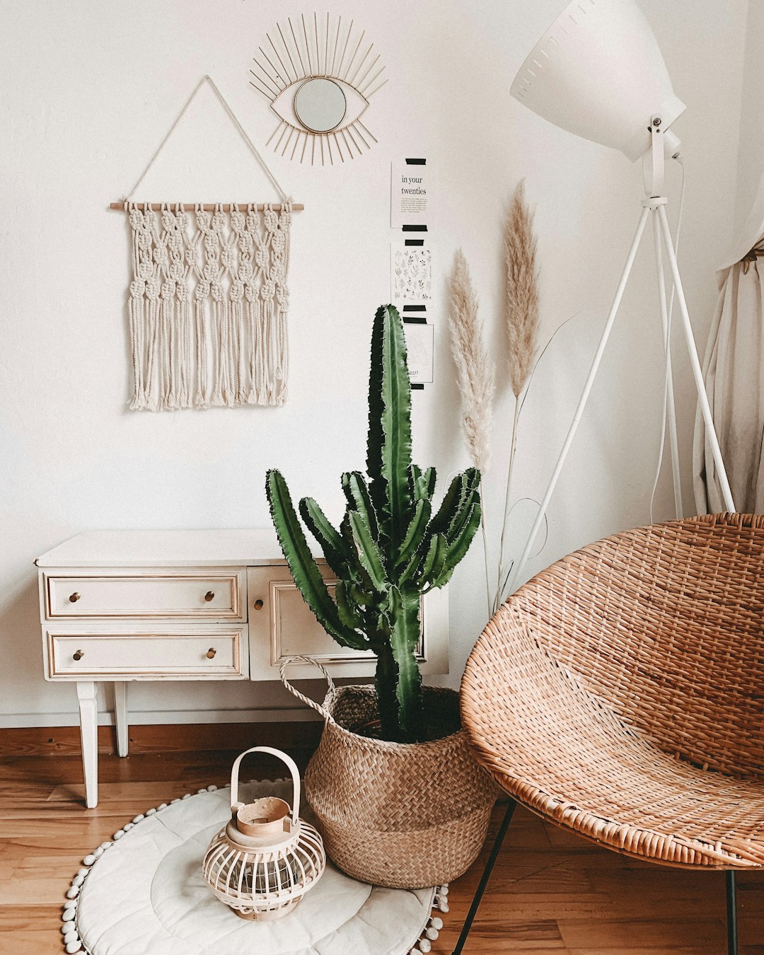 boho living room with macrame, rattan chair and cactus plant in a wicker basket on the floor. On the wall is a poster of the sun with a black frame hanging above a white sideboard. A white lamp stands next to it. The photo was taken using a Canon EOS R5 camera with a standard lens. –ar 51:64