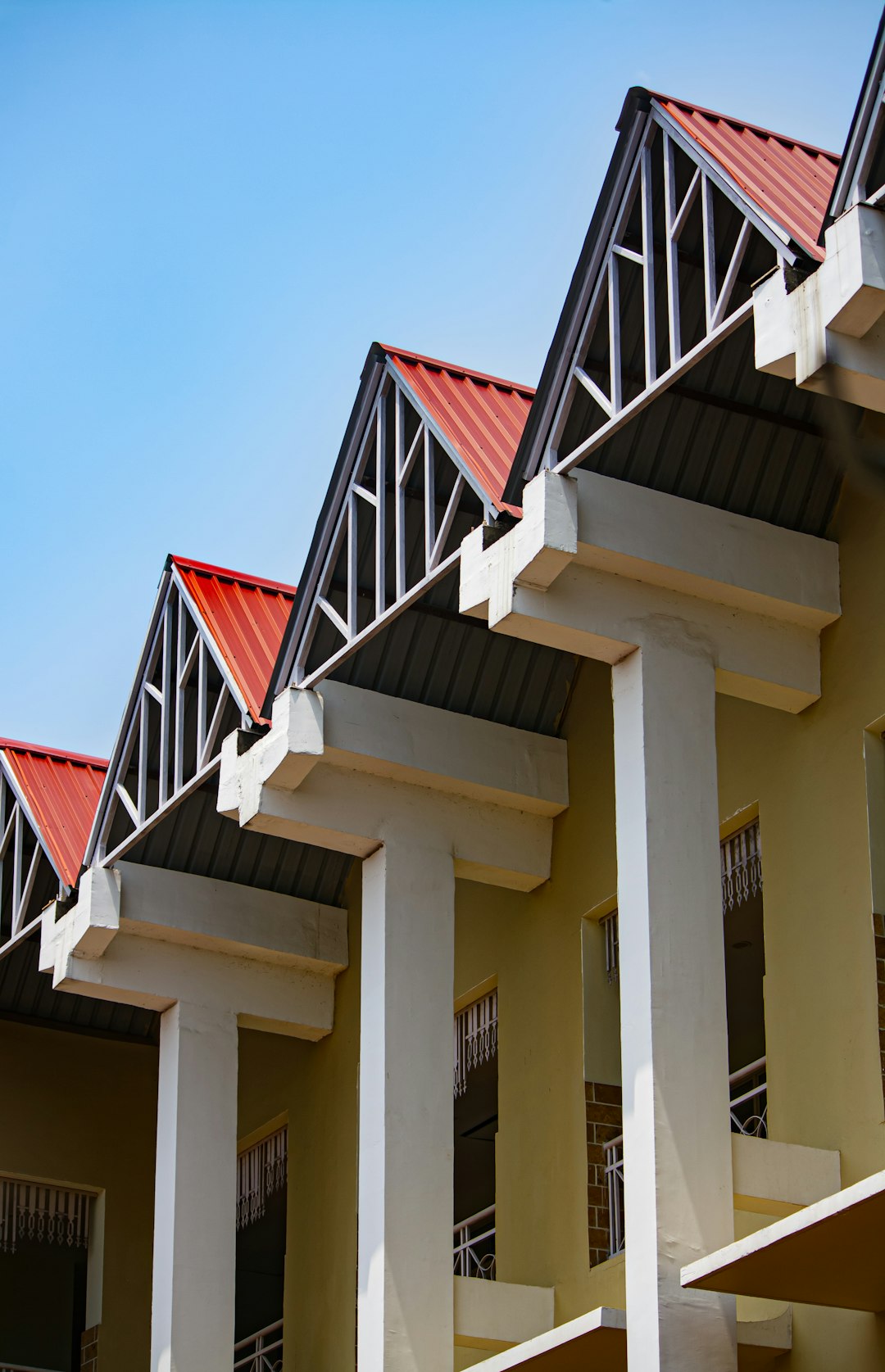 A row of houses with red roofs and white columns, steel beams on the eaves, flat walls, yellow concrete buildings, blue sky background, architectural photography, wide angle perspective, bright colors, modern architecture style in the style of telephoto lens, natural light. –ar 41:64