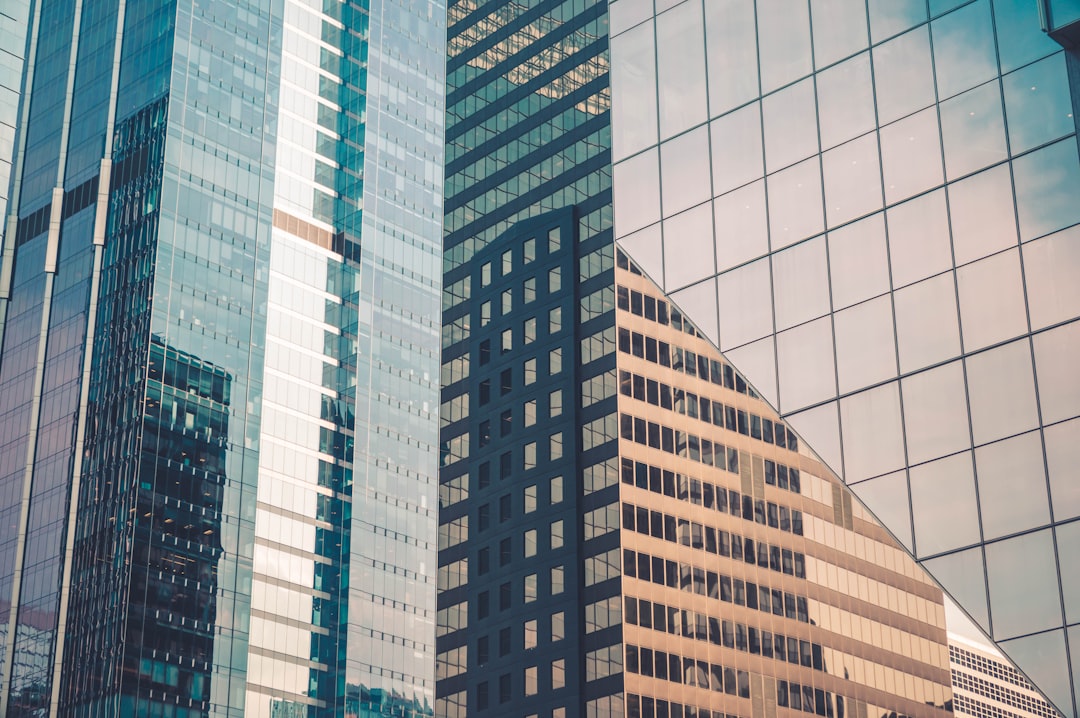 A photo of an office building with glass facades reflecting the surrounding buildings, showcasing modern architecture and urban life in New York City. The photograph captures the sleek lines and reflective surfaces that characterise contemporary skyscrapers. Taken on Canon EOS R5 at F2.8, ISO400, with a shutter speed of f/3.6. –ar 128:85