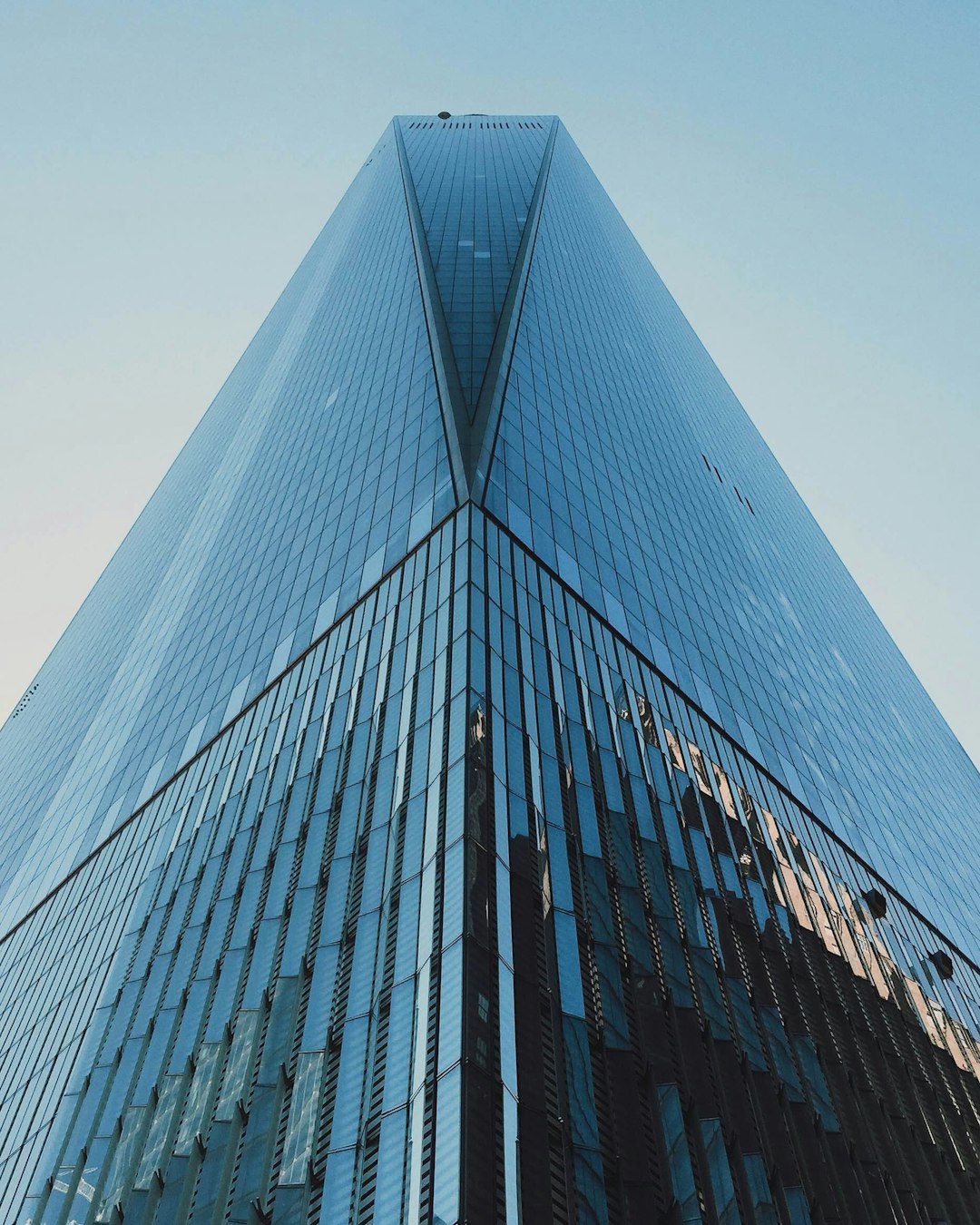 world trade center tower, wide angle shot, clear sky, low angle perspective, reflection on glass facade, sleek design, architectural photography, architectural appearance, modern architecture, glass and steel construction, blue tones, iconic building of New York City, skyline view. –ar 51:64