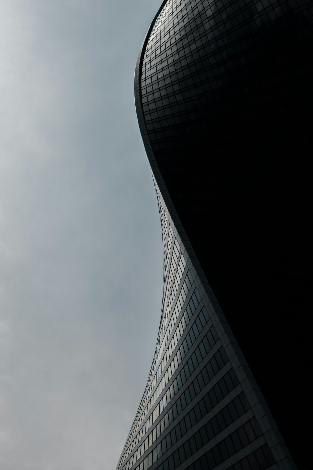 Black curved skyscraper against a gray sky. Closeup photography in the style of high resolution.