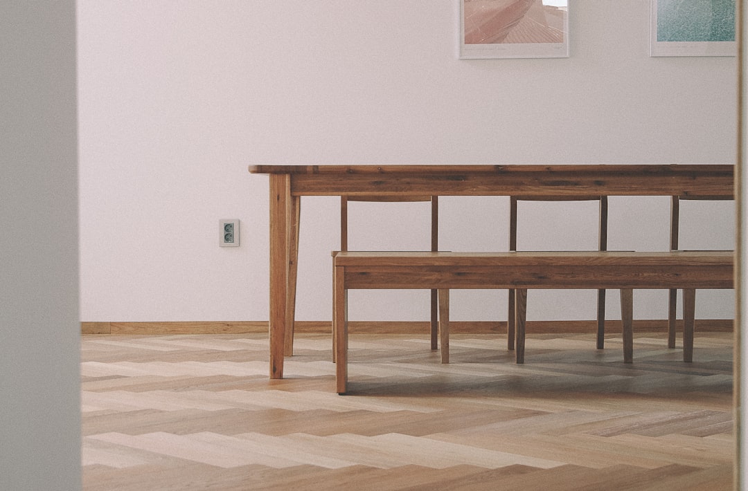 A photo of a large dining table and bench in an empty room with white walls, parquet floor with a herringbone wood pattern, natural light, muted colors, shot on a Canon EOS M50 Mark II camera in the style of minimal editing. –ar 32:21