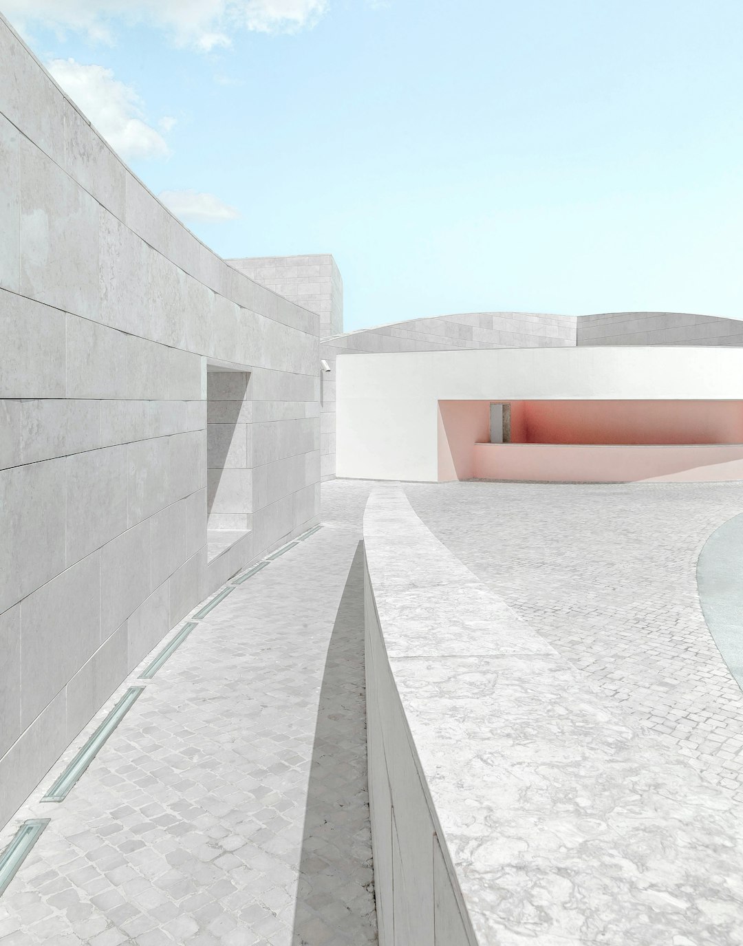 An architectural rendering of the facade and interior courtyard for an art gallery designed in the style of [Tadao Ando](https://goo.gl/search?artist%20Tadao%20Ando), a modern minimalist building in marble with pink details, located in Italy’s Cinquecento, overlooking a sea view, with a clean sky blue background, in a high angle shot, with straight lines, light grey tones, and detailed textures. –ar 25:32