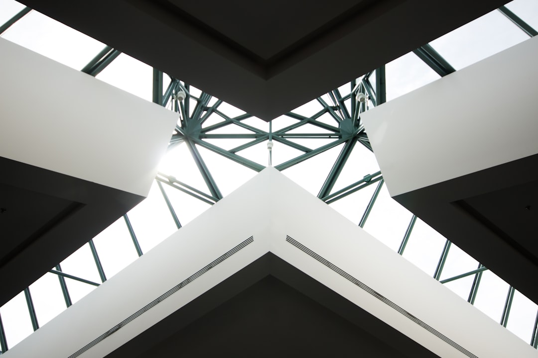 A geometric symmetrical photo of the ceiling and skylight, showcasing an angular structure with white walls and green steel beams. The perspective is from below looking up at the open space above, creating a sense of depth in light and shadow. High resolution, capturing intricate details for commercial photography. –ar 128:85