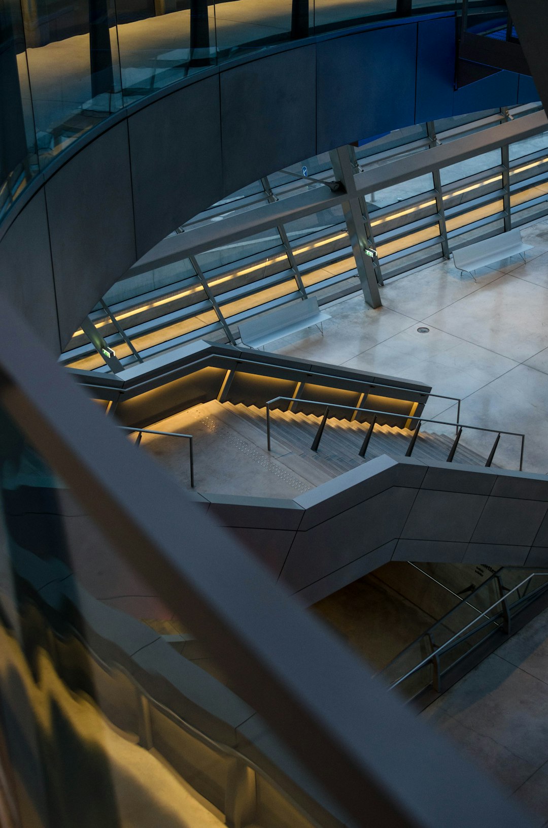 Closeup view of the curved staircase leading to an open square in front, with LED lights under each step and metal railings on both sides. The background is a modern building with glass curtain walls. In the evening light, it creates a warm atmosphere with soft tones. Photographed in the style of Sony A7s3 camera, with a focal length of F20, shutter speed of 5 meters, aperture of f/8, and iso6400.