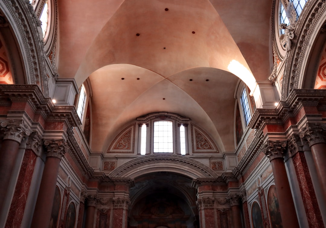 A photograph shows the ceiling and walls inside an old church in Rome, Italy. The space is bathed in warm sunlight that illuminates its rich redbrown stone walls with intricate architectural details. A tall arched vaulted roof appears to be made from natural light, as there is no lighting on it. In front stands an elegant baroque altar, and above it are two small stained glass windows. This scene captures a serene atmosphere, showcasing the grandeur of ancient architecture in the style of natural light. –ar 128:89