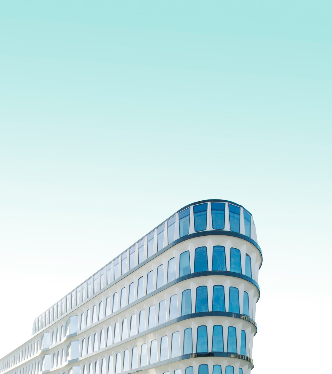 A curved modern building with blue windows on the right side of an isolated white background, in the minimalist style, flat design, high resolution photography, vibrant colors, natural light, professional color grading, clear and sharp focus, minimalistic details, modern aestheticism, high quality. –ar 113:128