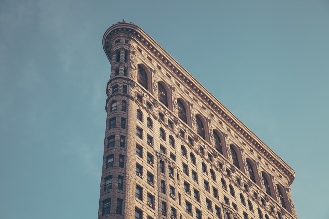 Flatiron Building, New York City, USA, in the style of vintage. A detailed photo of the iconic Flatiron Building against a clear blue sky. Soft focus on architectural details and windows, highlighting the historical architecture. Vintage color grading with soft pastel tones for an old-world charm effect. Low-angle shot showcasing the grandeur of the skyscraper, emphasizing its unique design and texture. –ar 128:85