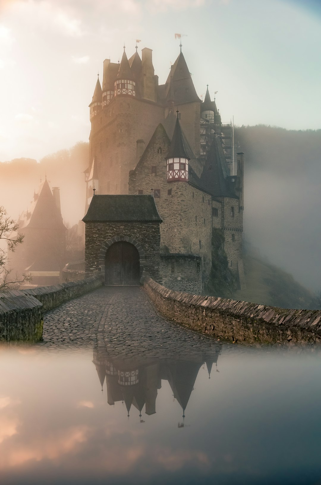 A medieval castle in a misty morning, with reflection on the water surface, surrounded by a foggy landscape, gothic architecture and stone walls, a large entrance gate, in the style of medieval fantasy, historical realism, photography. –ar 21:32