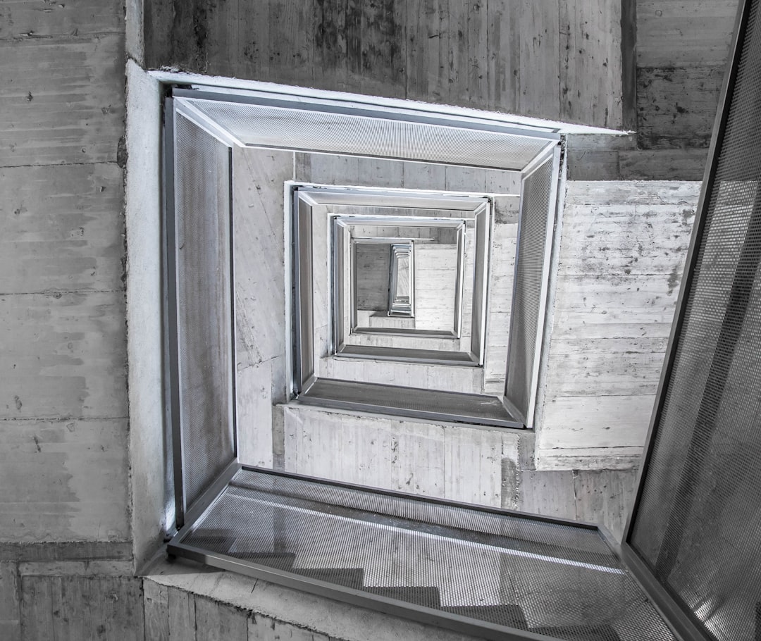 In the style of Tadao And była, an architectural photograph captures spiral staircases leading to different levels within concrete walls. The gray tones and symmetrical composition create depth in each square frame.