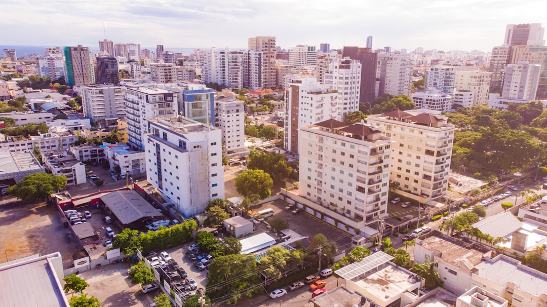 Aerial view of the city center in Barretos, facing buildings with white walls and gray roofs, surrounded by green trees, bustling streets filled with cars, tall skyscrapers standing beside modern apartment blocks, clear blue sky above, capturing urban life and architecture in the style of high-resolution photography, conveying vibrancy and energy of contemporary Barretos through vivid colors and sharp details in the cityscape. –ar 128:71