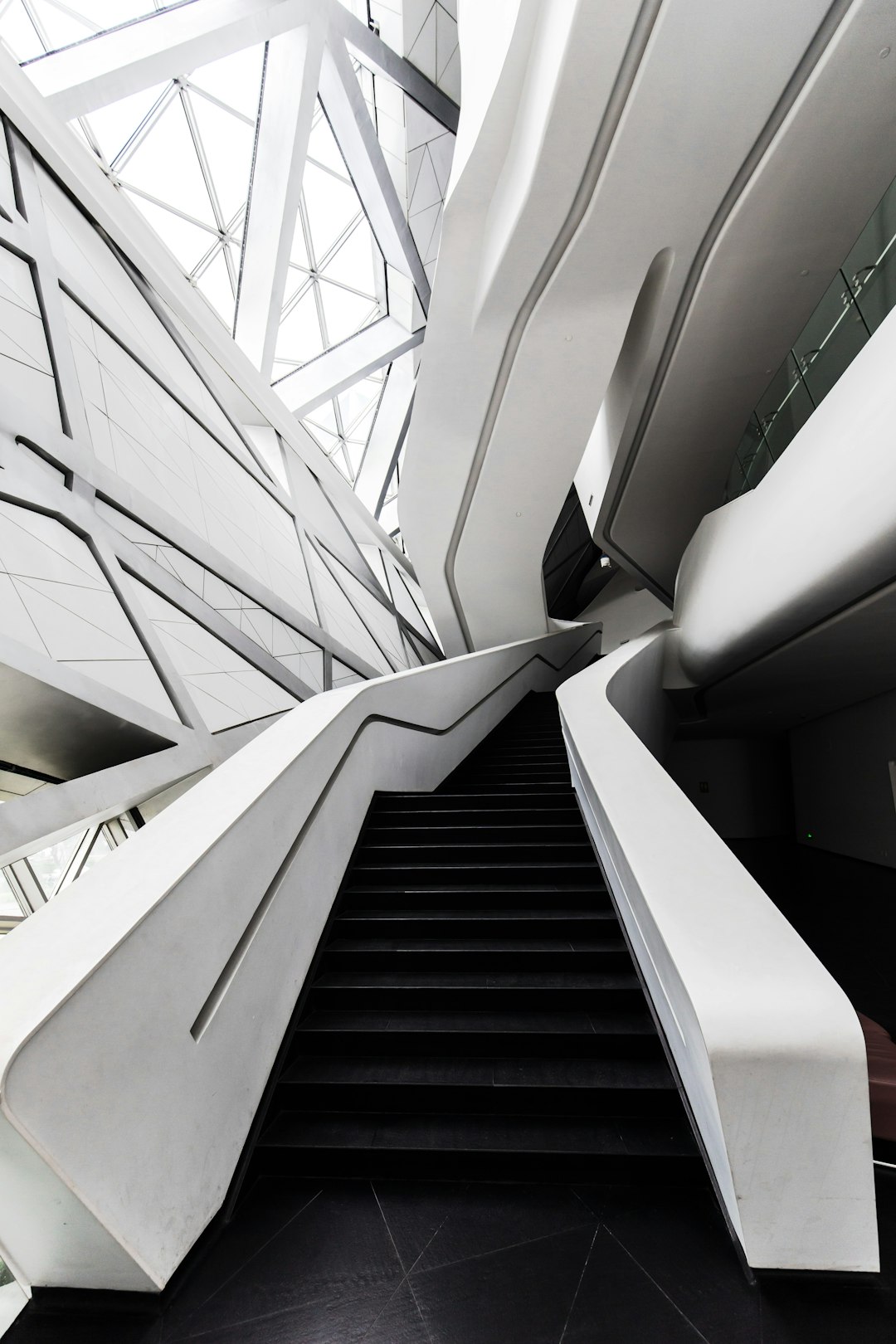 [Zaha Hadid](https://goo.gl/search?artist%20Zaha%20Hadid)’s white building interior with black stairs, geometric shapes, glass roof, and steel structure details. The photograph was taken in the style of the photographer in high definition. –ar 85:128