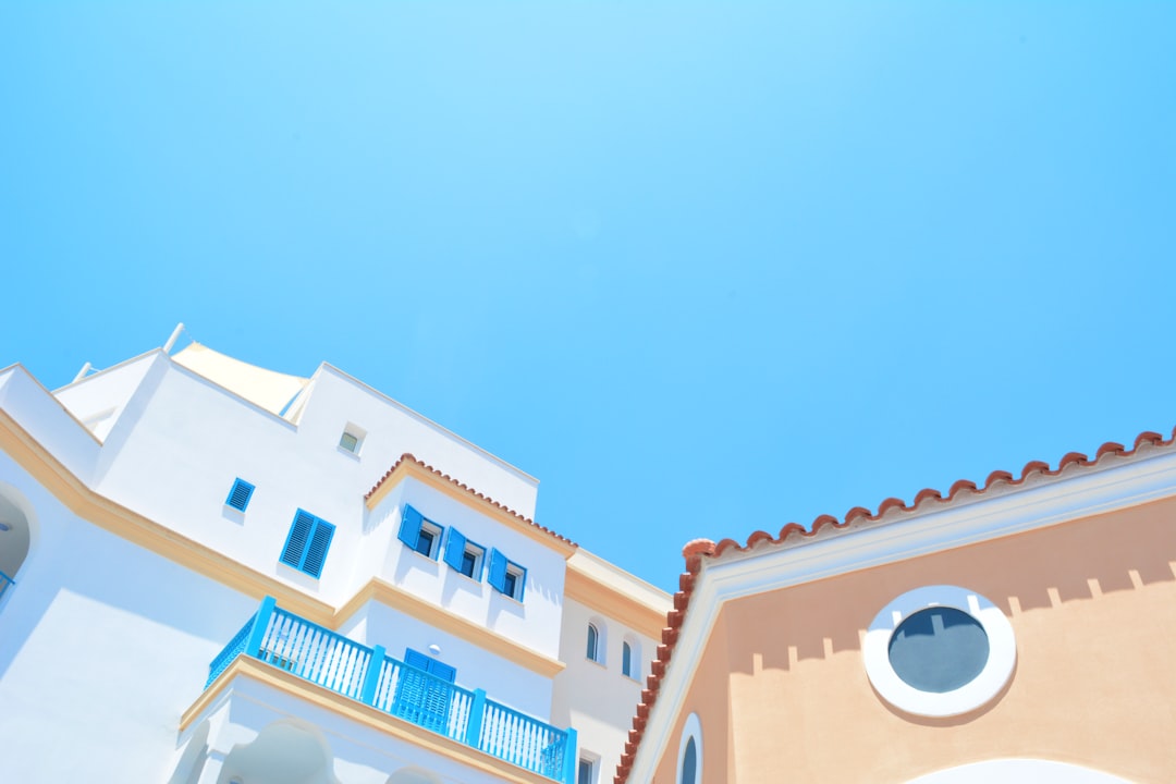 low angle photo of white and pastel buildings with blue accents, clear sky, warm colors, mediterranean style, sunny day, clean sharp focus, depth of field, f/28mm –ar 128:85