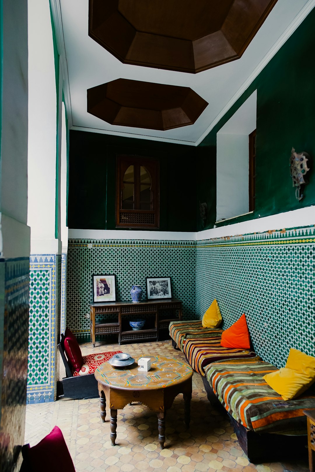 Marrakech, interior design in an old house with green walls and tiles, big table, colorful sofa, red yellow blue pillows, black roof ceiling with wooden skylight, photography in the style of Fujifilm Pro 400H. –ar 85:128