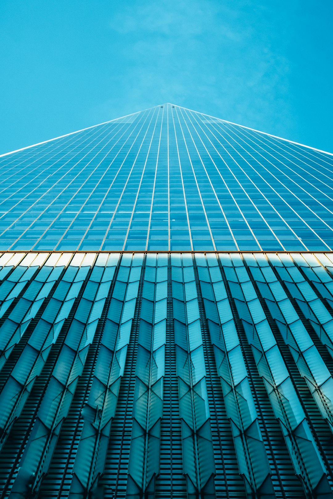 A photograph of the outside of an office building with blue glass and metal, symmetrical, looking up at it from below at the tall skyscraper. The photograph is ultra realistic in the style of architectural photography, with professional color grading, soft shadows, minimal contrast, and clean sharp focus in the style of magazine style photography. –ar 85:128