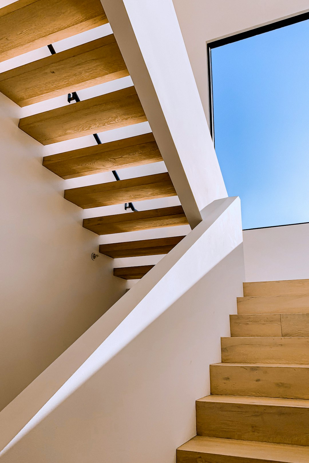 Staircase with white walls and light wood, open space on the top floor of modern home, closeup view of stairs, window at side showing blue sky, natural lighting, interior design photography, in the style of Nikon D850.