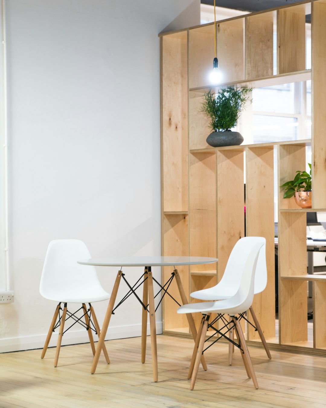 A minimalist, Scandinavian style office space with light wood accents and white walls, featuring two chairs in the style of Eames around an elegant glass table. The room includes built-in wooden shelves for storage, creating the perfect blend of functionality and simplicity in urban London’s trendy neighborhood. Photography, using a Canon EOS R5 camera with a macro lens to capture intricate details on both the furniture and decor elements.