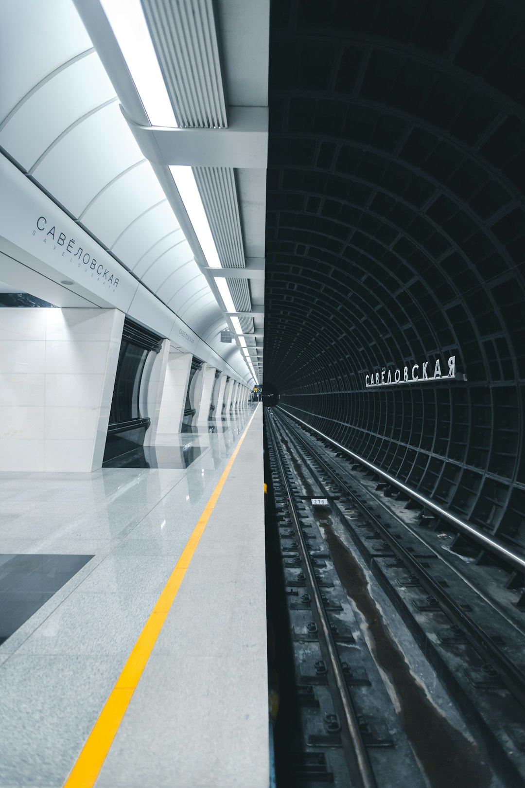 modern minimalistic underground station in moscow, white and grey colour scheme, straight lines, yellow details, “carl utmost” written on the wall above the tracks, unsplash photography style,