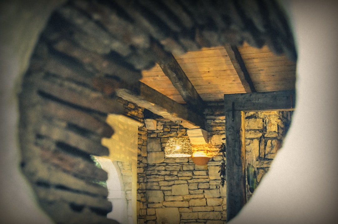 Closeup of the interior wall of an old stone house with wooden beams, seen through a circular mirror, creating a romantic and mysterious atmosphere with a blurred background. –ar 128:85