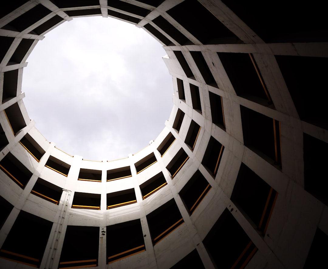 Photo of circular white steel structure with a skylight, looking up from the ground. Architecture photography in the style of brutalism.