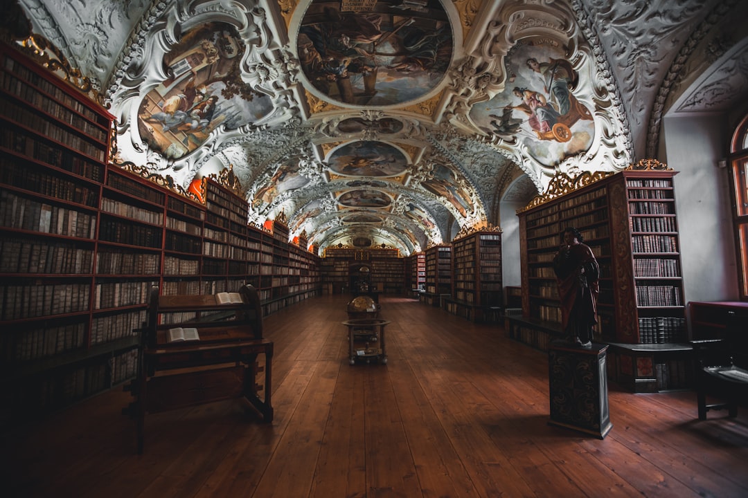 Photo of the interior of an old library in Prague, with wooden floors and ceiling painted with frescoes, many bookshelves filled with books, and statues on display. The photo was taken in the style of professional photographers using a Sony Alpha A7 III camera and Zeiss Batis lens 85mm f/2.