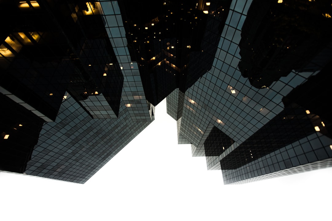 A photo of two skyscrapers from below, their reflections creating an illusion that they form one building, taken with a Canon EOS camera and lens at an f/28 aperture setting. The photograph was taken in the evening against a white background, with a focus on sharp details and high contrast between light and shadow.