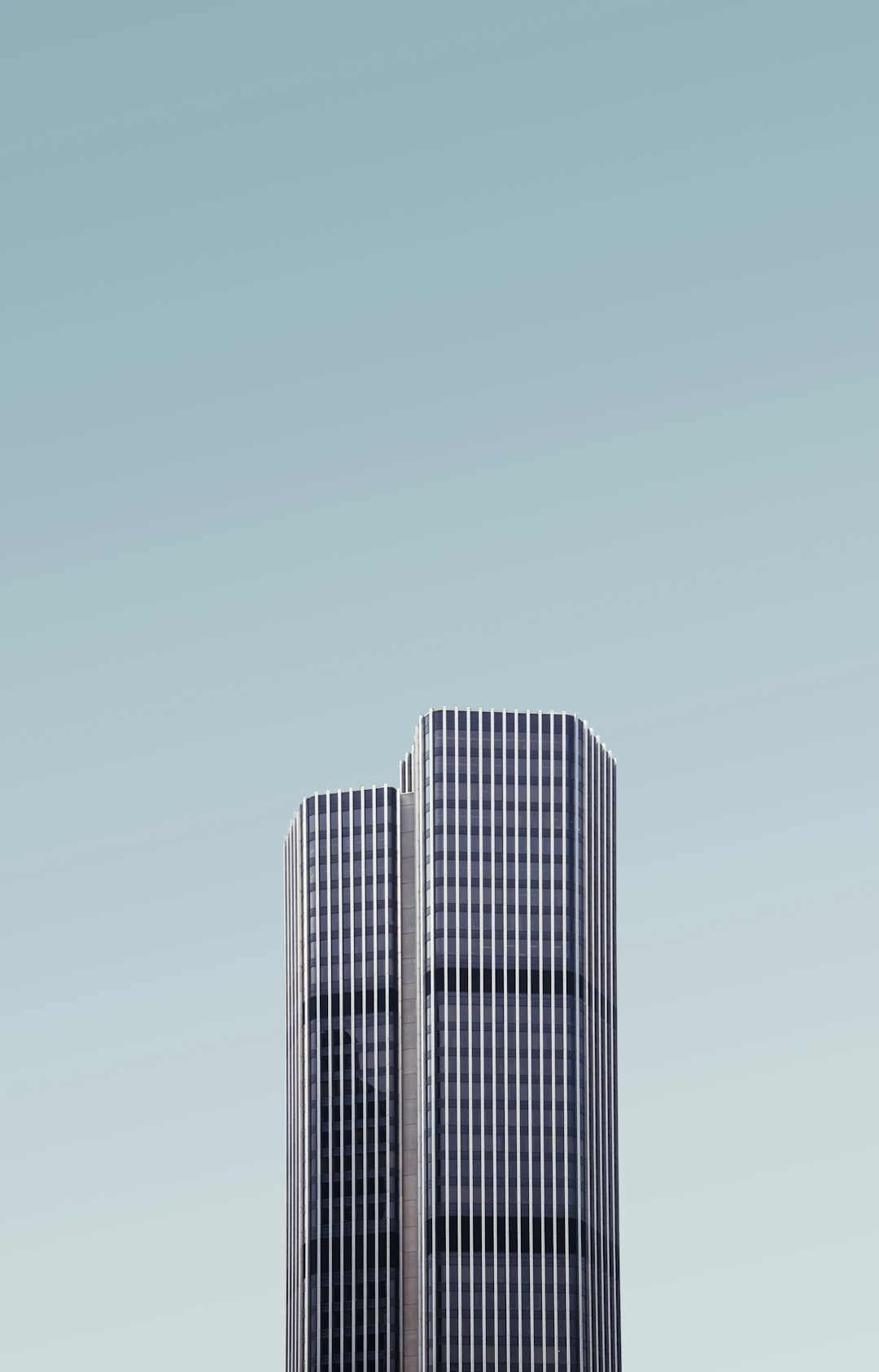 A minimalist photo of two skyscrapers, with the top part showing a flat blue sky and the bottom parts having vertical lines forming an architectural shape in the style of modern minimalism with soft tones and a high resolution with no shadows, shot with a Sony Alpha A9 II camera and Cinestill 400 film.