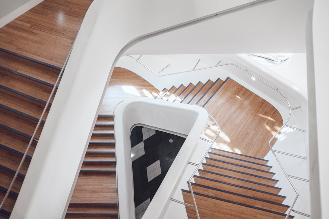 A staircase in the lobby of an office building, white and wood, closeup view from above, in the style of modern style, geometric shapes, curved lines, natural light, architectural photography, Canon EOS R5, wideangle lens, interior design detail, wooden floor.