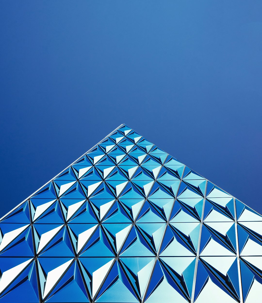 a photo of the facade made from blue glass with triangular pattern, on clear sky background, close up, low angle shot, high resolution photography –ar 55:64