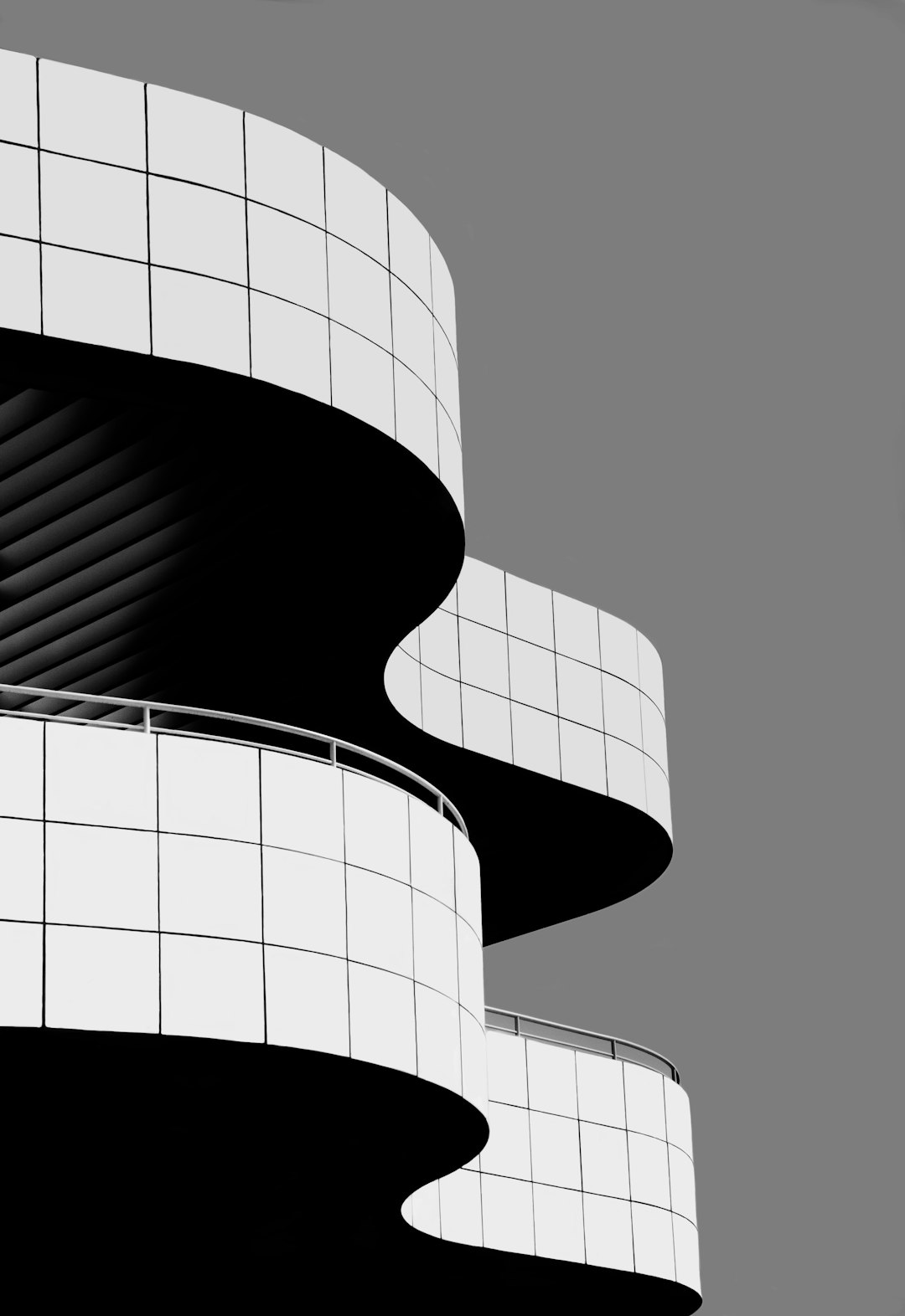 A close-up black and white photo of the curvilinear architecture of The MET in Los Angeles, capturing its modern design with geometric shapes, clean lines, and minimalist detailing. The building’s exterior features large balconies and curved edges, creating an elegant silhouette against a clear sky. This architectural photography composition highlights symmetry and simplicity, emphasizing form over color. The photo is in the style of minimalist architectural photography, focusing on the building’s clean lines and geometric forms.