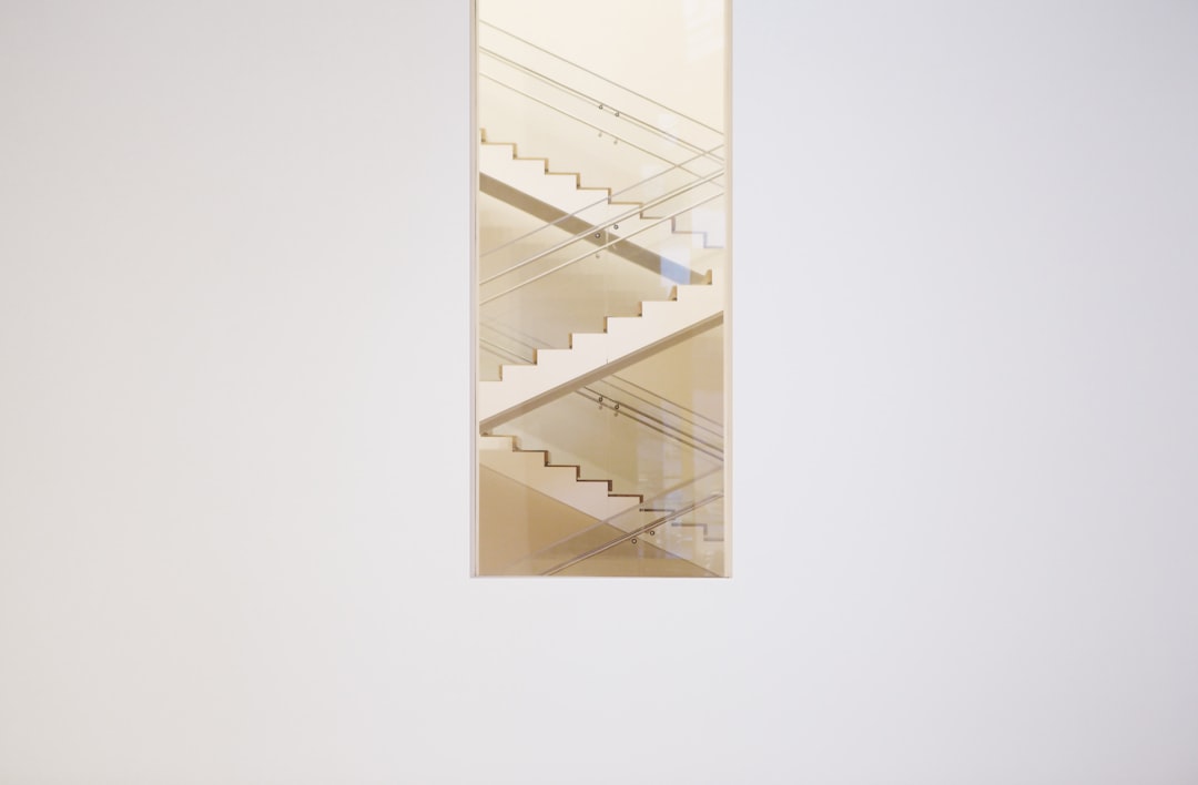 A vertical rectangle on the wall of an art gallery, featuring three modern white staircase blocks stacked vertically with glass railings, against a plain background. The stairs and railings have subtle reflections in light beige tones, creating a minimalist aesthetic. The artwork is in the style of modern abstract artist.