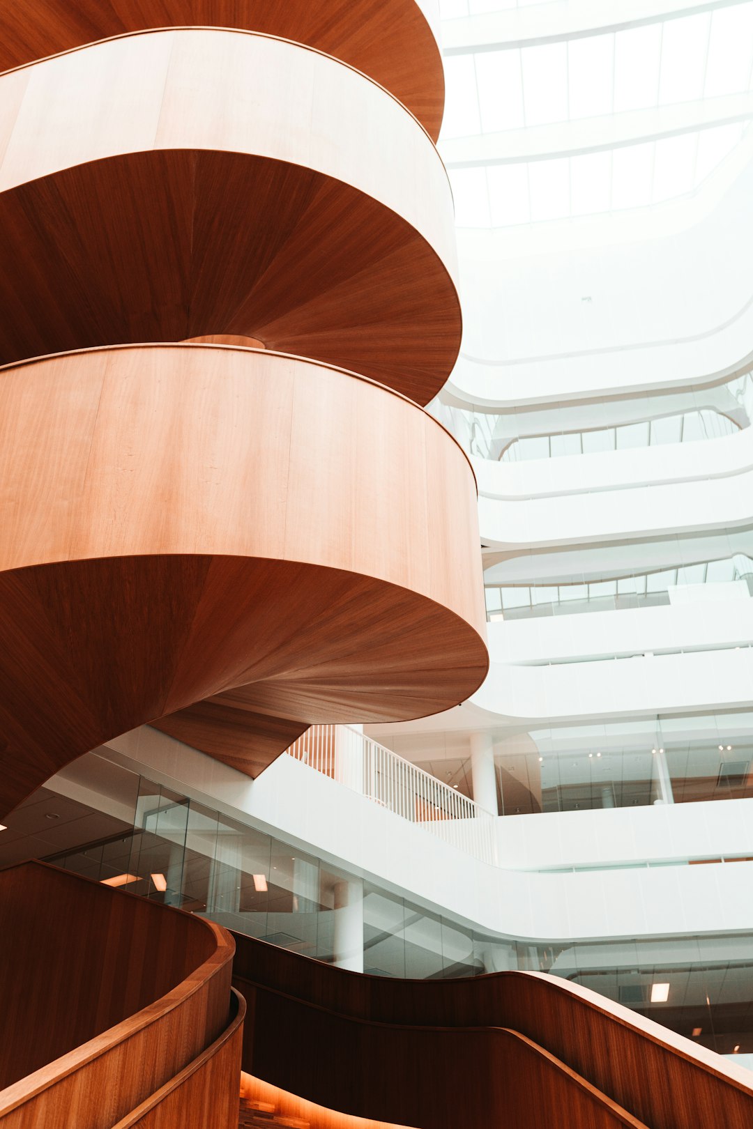 A photo of an interior modern building with wood and white details, a large wooden spiral staircase in the middle, natural light, shot in the style of canon eos r5.