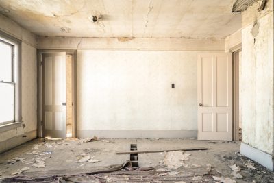 A photograph of an empty room in the process of being styled in the style of Antarctica, with white walls, no windows, an open door, peeling wallpaper, a peeling ceiling, debris on the floor, shot with a Sony Alpha A7 III, using natural light, neutral tones, at a high resolution, with a hyper realistic style.