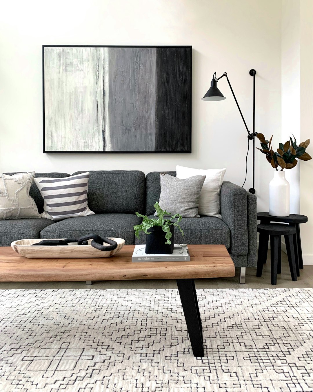 modern living room with grey couch, black and white rug, wooden coffee table, abstract art on wall above sofa, black metal floor lamp, side tables with vases of greenery, simple yet elegant home decor –ar 51:64