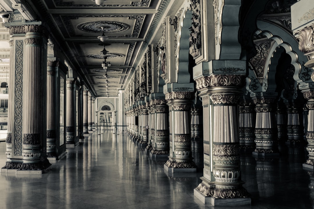 An ornate hallway with columns and arches of an Indian palace in Mysore, India, detailed in the style of monochrome photography. A long corridor lined with intricate pillars adorned with patterns, photorealistic landscapes in the style of dark white and light gray, high resolution. –ar 128:85