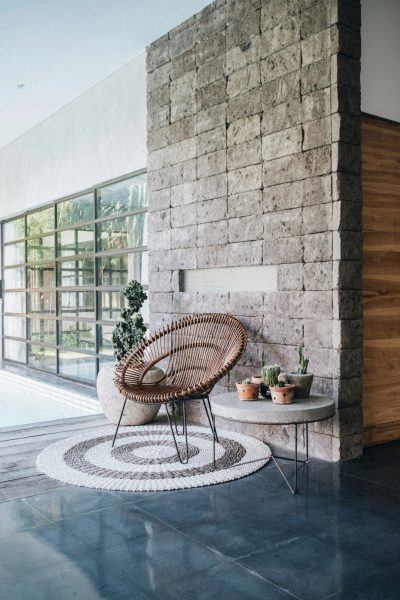 modern interior design, accentual, subtle, large stone wall with round rug on the floor and small table in front of it, cacti plant, modern chair made out of rattan, natural light, shot in the style of Canon EOS1D X Mark III