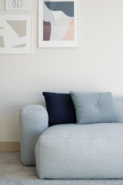 A close-up photo of a sofa in a light grey color with a dark blue pillow. Minimalistic interior design with three abstract posters on the wall above it. Scandinavian style with neutral colors and a soft daylight for a natural look.