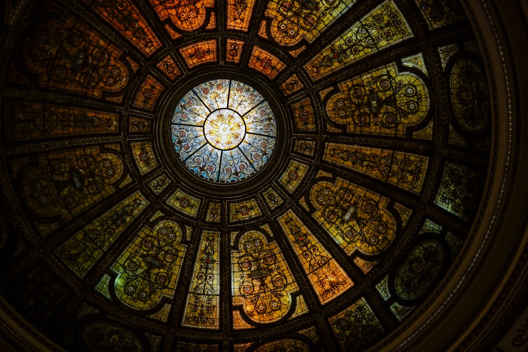 stained glass dome ceiling, illuminated by sunlight, viewed from the inside of an old art deco building in Chicago with ornate details and decorative patterns, cinematic, high resolution, with a Bokeh effect, very detailed, professional photography with professional color grading, depth of field to show intricate detail, HDR, in the style of various artists. –ar 128:85