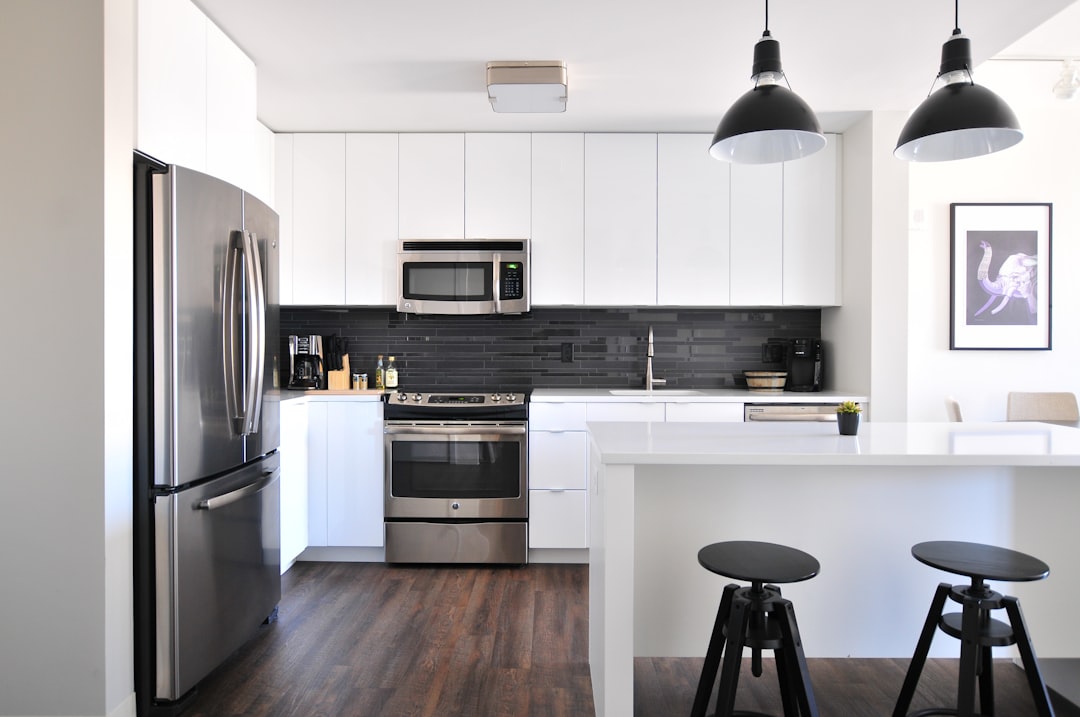 Minimalist white kitchen with stainless steel appliances, black accent lighting and wood flooring –ar 128:85